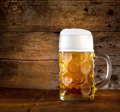 Bierkrug mit goldgelbem Bier und Schaumkrone vor rustikalem Holzhintergrund