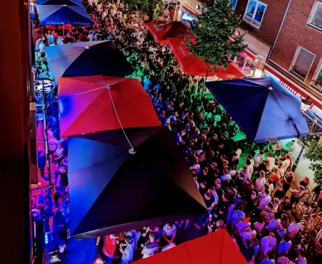 Blick von oben auf eine dicht gedrängte Party in der Düsseldorfer Altstadt mit vielen Gästen, bunten Lichtern und großen ASTRA-Schirmen vor der Gastronomie.