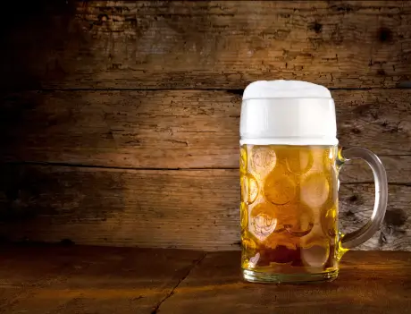 Biergläser mit goldenem Bier auf einem rustikalen Holztisch als Motiv für das ganzjährige Oktoberfest.